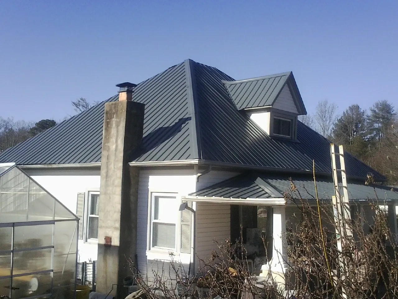 Dark blue standing seam metal roof on a white farmhouse with dormer — Slate & Tile Roof Repair by Roofing Brothers in Bee Spring