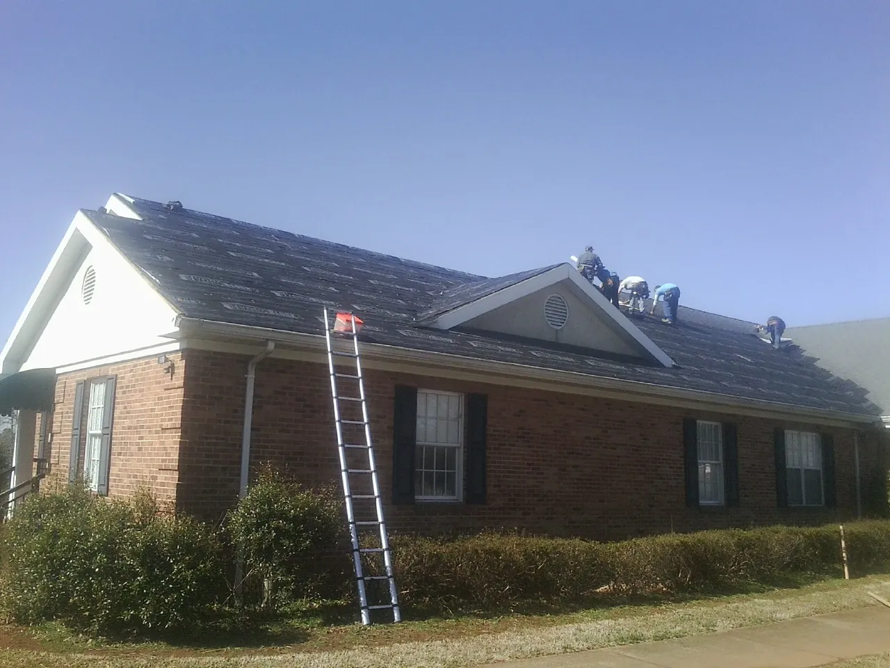 Crew tearing shingles off a brick ranch roof with a ladder set — Metal Roof Repair work by our crew in Bee Spring