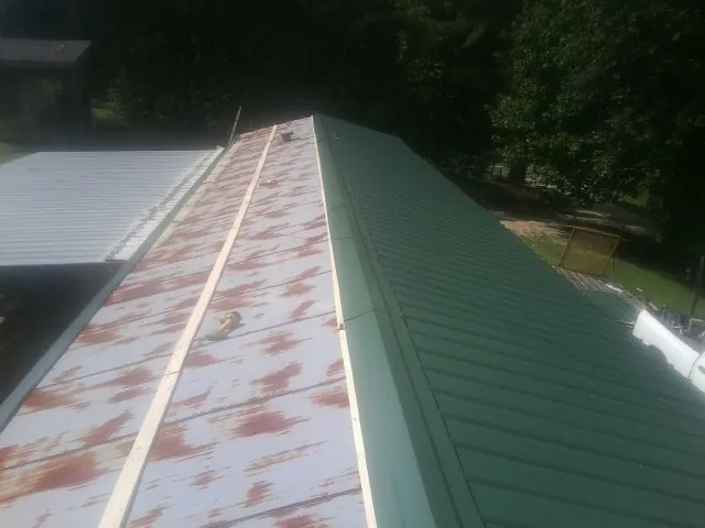 Old rusted panels beside newly installed green metal roofing — Wind Damage Roof Repair by Roofing Brothers in Bee Spring