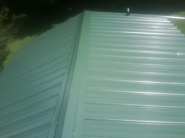New green metal panels meeting at the ridge of a roof — Flat Roof Repair work by our crew in Bee Spring