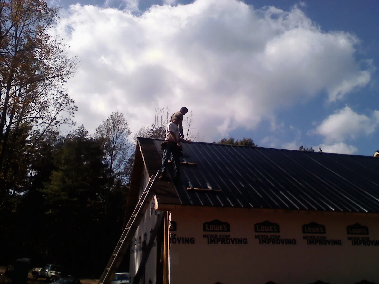 Roofer fastening dark metal panels high against a cloudy sky, from a Roof Inspection job in Bee Spring