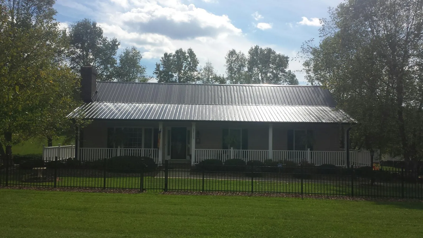 Gray metal roof on a brick ranch with a full width front porch — Gutter Guard Installation work by our crew in Bee Spring