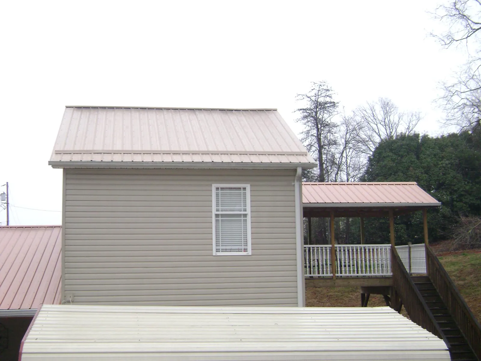 Tan metal roofs on a two story addition and attached porch, from a Roof Replacement job in Bee Spring